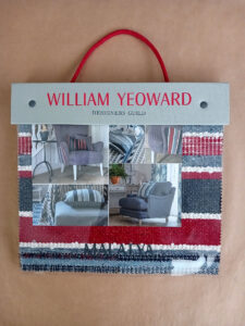 Catálogo de tecidos de William Yeoward - Designers Guild - representados pela By Tri Brands - na capa aparecem 4 poltronas com tecidos predominantemente cinzas com almofadas com estampas listradas com cinzas, vermelhos, brancos e azuis.